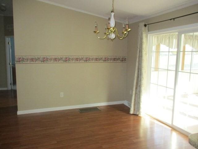 empty room featuring ornamental molding, dark wood-type flooring, and a notable chandelier