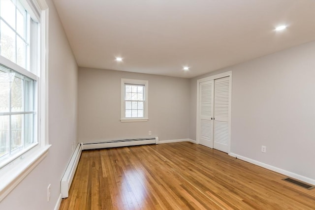 spare room featuring baseboard heating and light hardwood / wood-style flooring