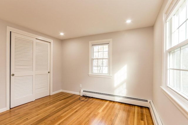 unfurnished bedroom featuring light hardwood / wood-style floors, a baseboard radiator, and a closet