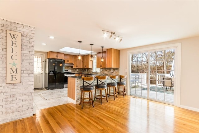 kitchen with backsplash, black fridge, hanging light fixtures, light wood-type flooring, and a breakfast bar area