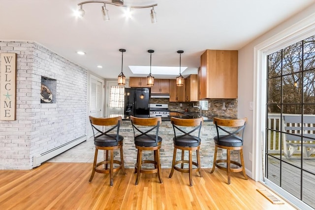 kitchen featuring a baseboard heating unit, pendant lighting, white range with gas cooktop, black fridge with ice dispenser, and light wood-type flooring