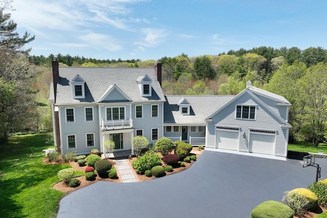 view of front of home with a chimney, a front yard, a balcony, a garage, and driveway