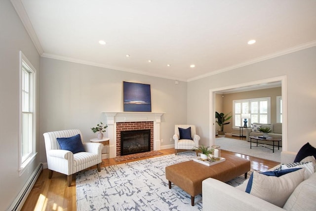 living area with light wood-style flooring, baseboard heating, ornamental molding, a brick fireplace, and baseboards