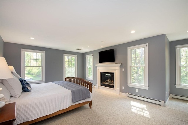 bedroom with light carpet, multiple windows, baseboard heating, and a glass covered fireplace