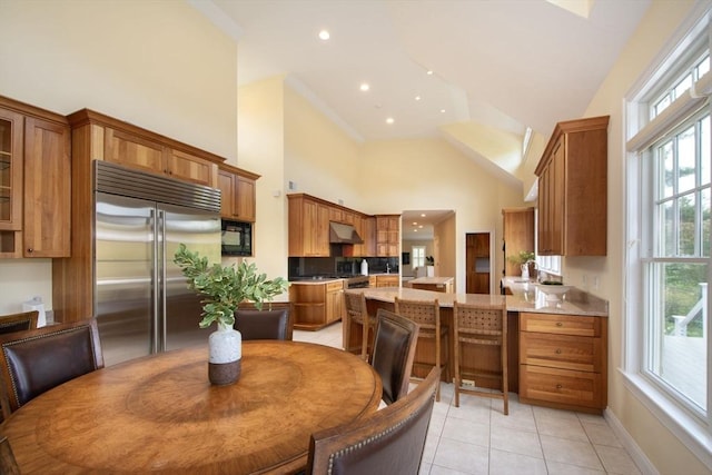 kitchen featuring brown cabinetry, a peninsula, stainless steel built in refrigerator, under cabinet range hood, and black microwave