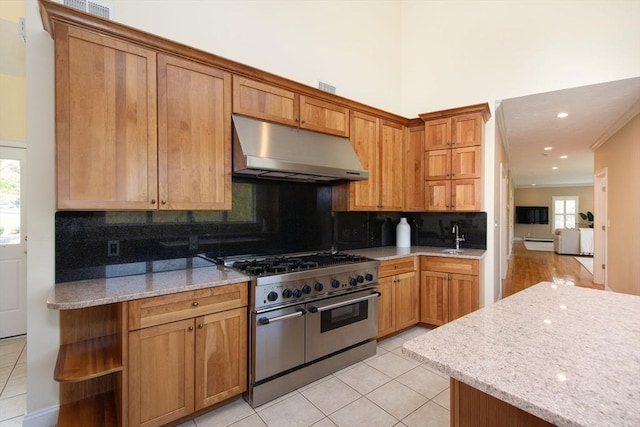 kitchen with light tile patterned floors, light stone counters, under cabinet range hood, double oven range, and tasteful backsplash