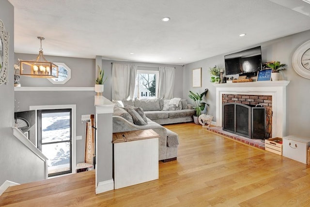 living room featuring a brick fireplace, a notable chandelier, and light wood-type flooring