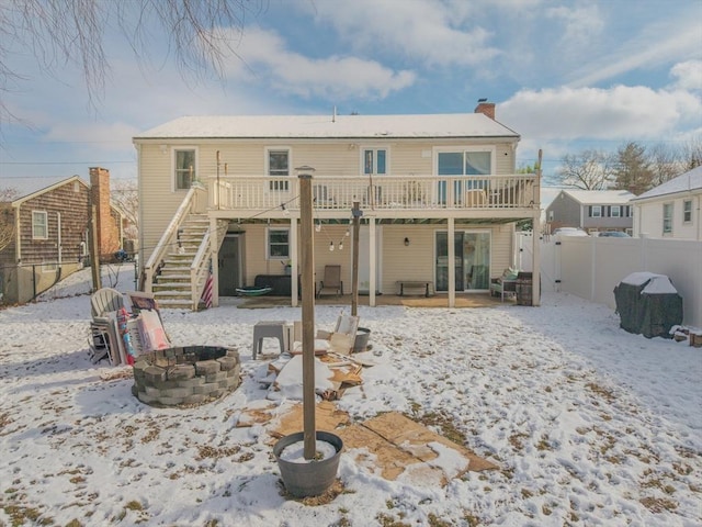 snow covered rear of property with a wooden deck and a fire pit