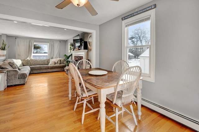 dining room featuring a baseboard radiator, ceiling fan, a fireplace, and light wood-type flooring