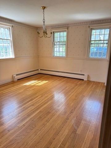 empty room featuring a baseboard heating unit, wood finished floors, a notable chandelier, and wallpapered walls
