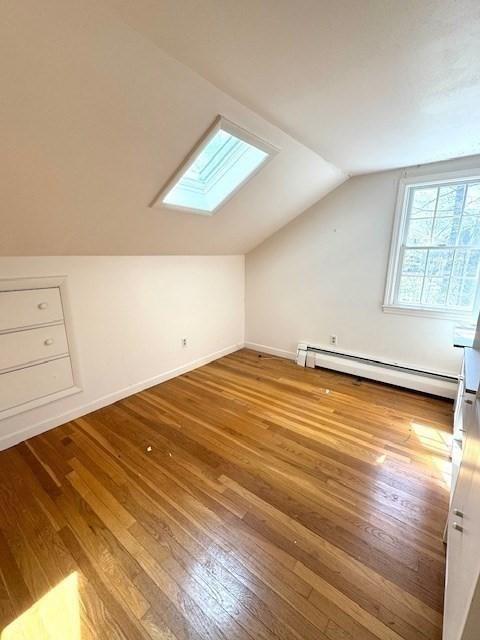 bonus room featuring hardwood / wood-style flooring, a baseboard heating unit, baseboards, and lofted ceiling with skylight
