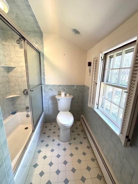 full bathroom with tile walls, a wainscoted wall, tile patterned floors, a baseboard heating unit, and combined bath / shower with glass door