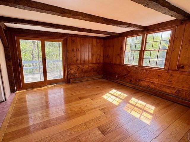 spare room featuring light wood-style flooring, wood walls, beam ceiling, and a wealth of natural light