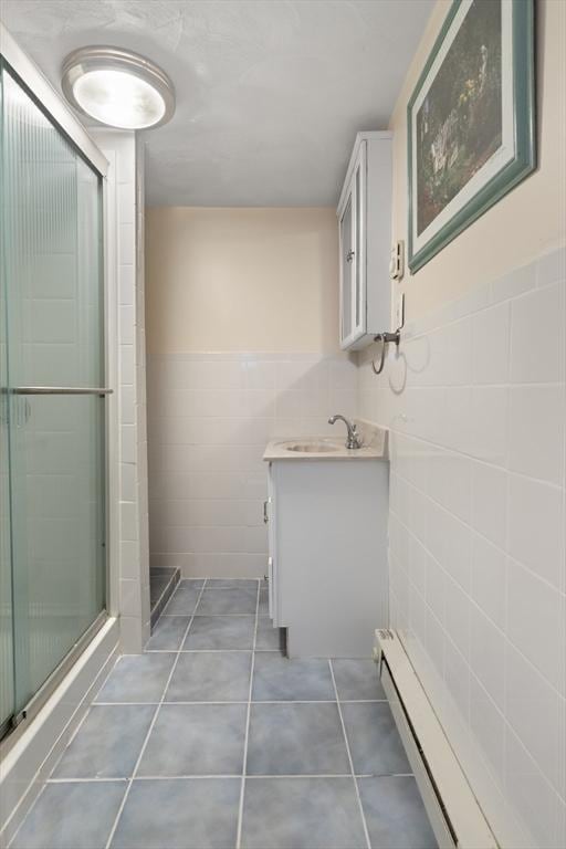 bathroom with a shower with shower door, tile walls, vanity, a baseboard heating unit, and tile patterned floors