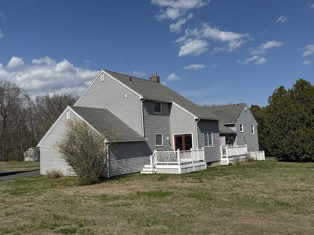 rear view of property with a lawn, a shingled roof, a chimney, and a deck