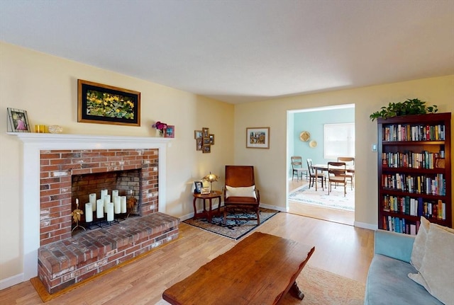 living room featuring baseboards, a brick fireplace, and wood finished floors