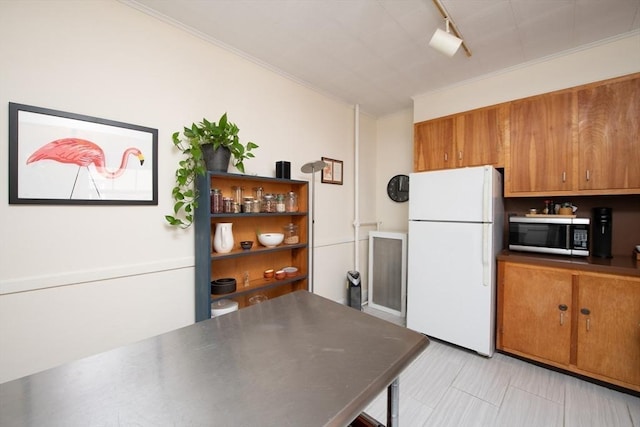 kitchen with brown cabinetry, stainless steel microwave, crown molding, and freestanding refrigerator