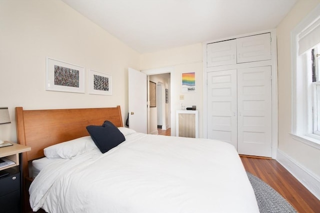 bedroom with a closet, multiple windows, baseboards, and wood finished floors