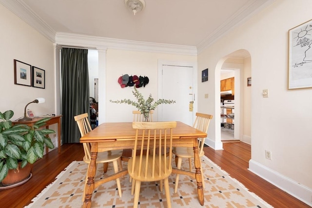 dining room with crown molding, light wood-style flooring, baseboards, and arched walkways