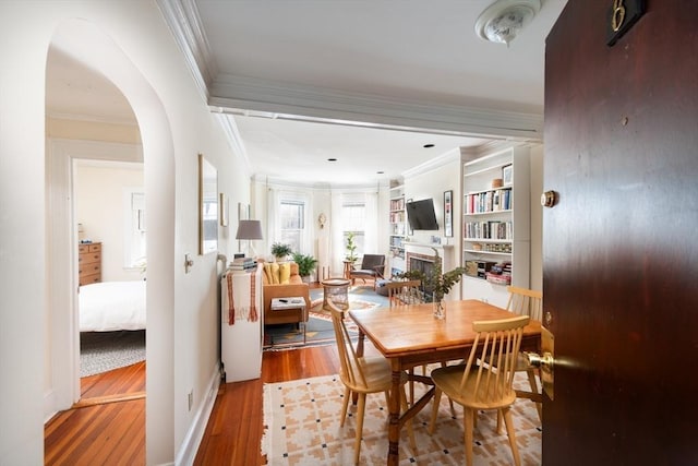 dining room featuring a fireplace, crown molding, wood finished floors, and arched walkways