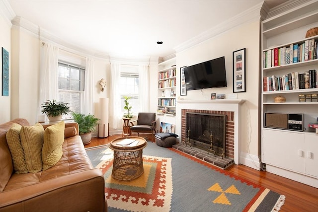 living area with a fireplace, crown molding, built in shelves, and wood finished floors