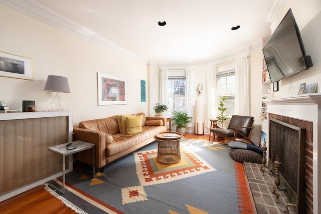 living area with a brick fireplace, wood finished floors, and crown molding