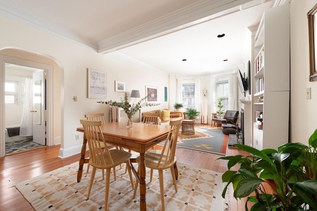 dining space with baseboards, arched walkways, light wood finished floors, and ornamental molding