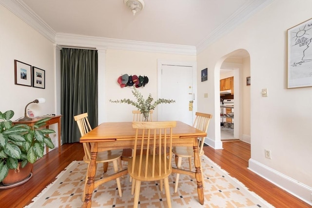 dining room featuring baseboards, arched walkways, crown molding, and light wood finished floors