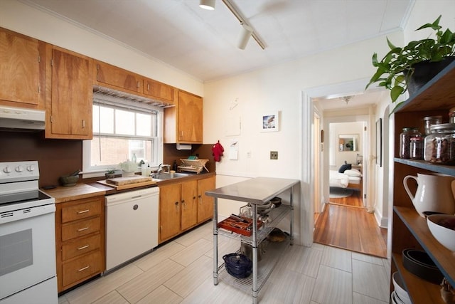 kitchen with track lighting, under cabinet range hood, brown cabinetry, white appliances, and a sink