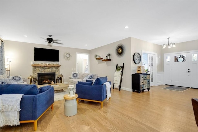 living room featuring a fireplace, ceiling fan with notable chandelier, and light wood-type flooring