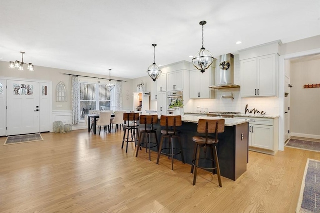 kitchen with white cabinetry, wall chimney exhaust hood, and an island with sink