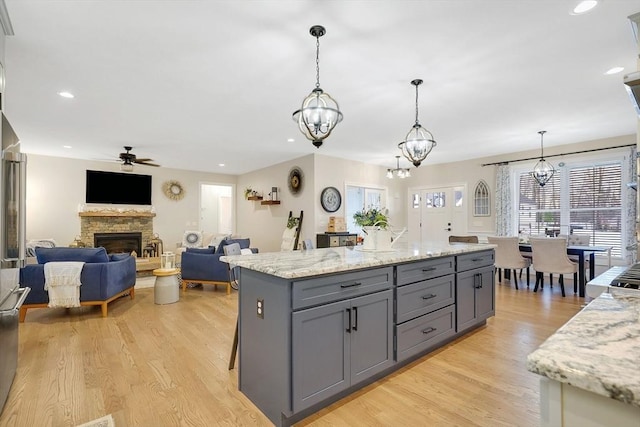 kitchen featuring gray cabinetry, light stone counters, hanging light fixtures, light wood-type flooring, and a kitchen island