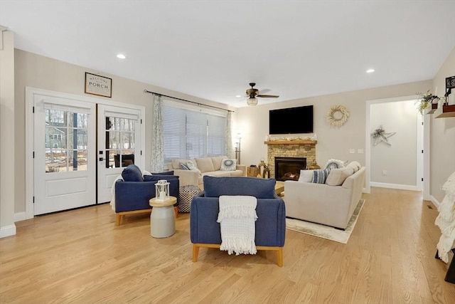 living room featuring a stone fireplace, french doors, ceiling fan, and light wood-type flooring