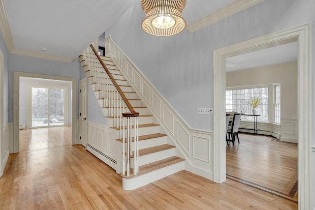 stairway with a decorative wall, wood finished floors, crown molding, and a baseboard radiator