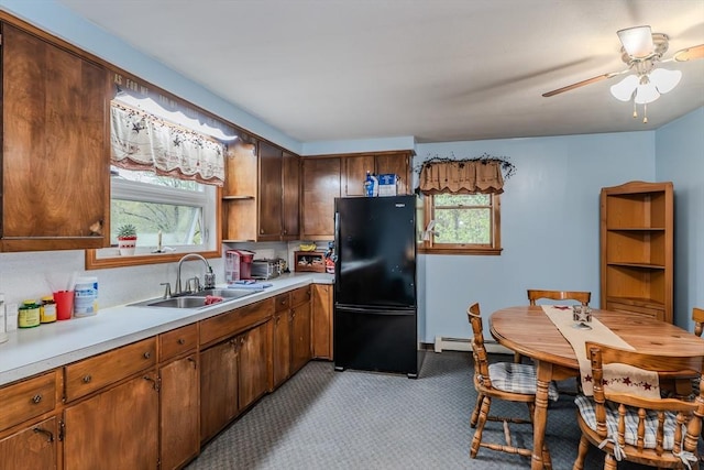 kitchen featuring freestanding refrigerator, a sink, a baseboard heating unit, light countertops, and a ceiling fan
