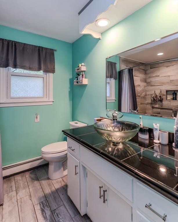 bathroom with a baseboard heating unit, toilet, vanity, wood finished floors, and a shower with shower curtain