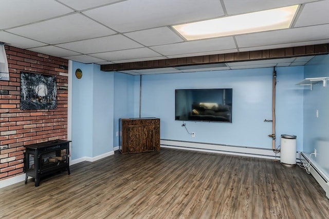 finished below grade area with a wood stove, baseboards, wood finished floors, baseboard heating, and a baseboard heating unit