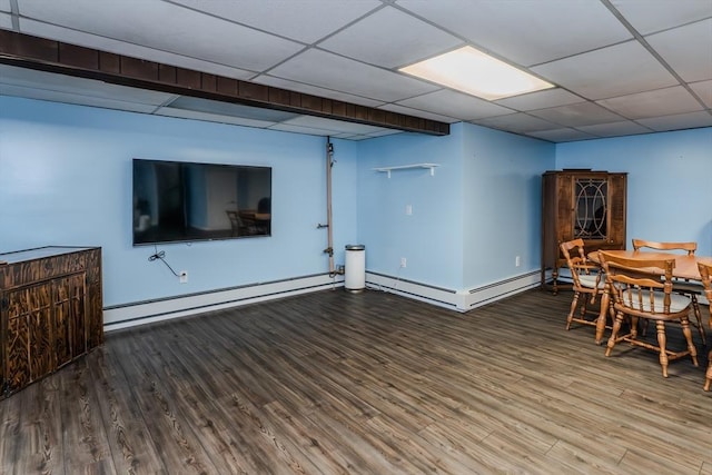 below grade area featuring wood finished floors, baseboards, a drop ceiling, and a baseboard heating unit