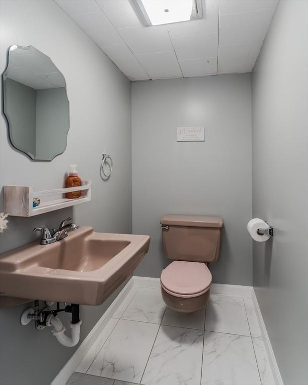 bathroom with marble look tile flooring, baseboards, toilet, and a sink