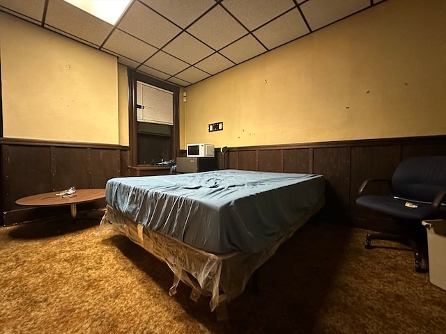 bedroom with wood walls, carpet flooring, and a drop ceiling