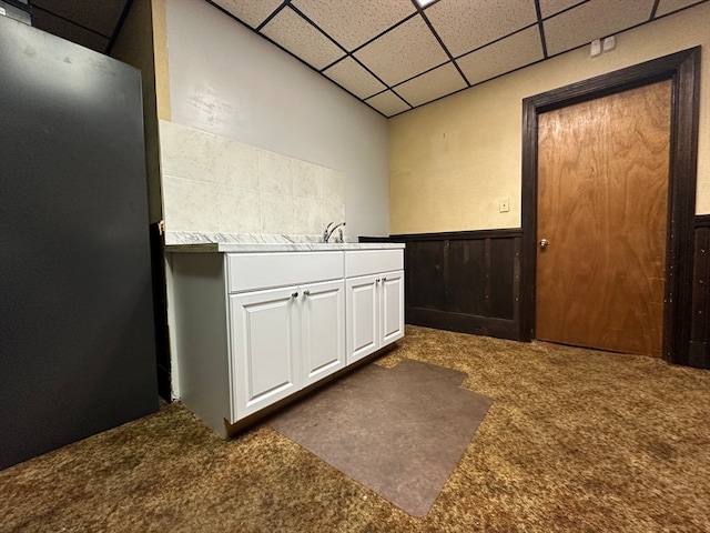 interior space with white cabinetry, wood walls, a paneled ceiling, and dark carpet