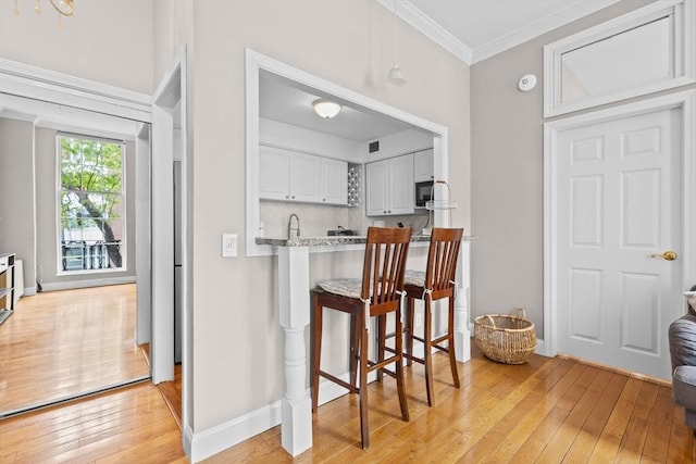 17 Bowdoin Unit 2B, Boston, MA 02114 - kitchen with light wood-type flooring, ornamental molding, black microwave, a breakfast bar area, and decorative backsplash