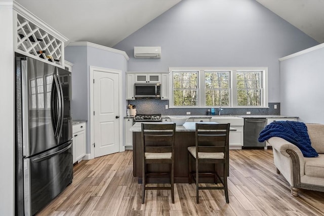 kitchen featuring an AC wall unit, a center island, white cabinetry, stainless steel appliances, and a kitchen breakfast bar