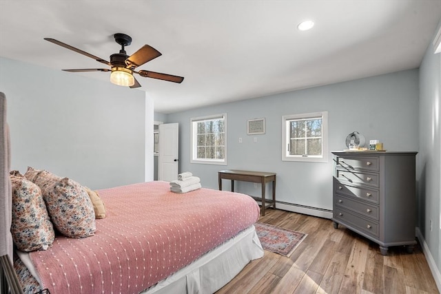 bedroom featuring ceiling fan, a baseboard heating unit, light hardwood / wood-style floors, and multiple windows