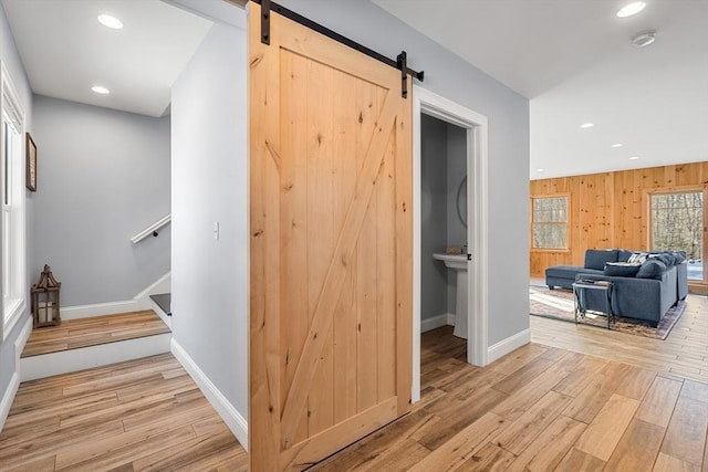 corridor with a barn door, wooden walls, and light hardwood / wood-style floors