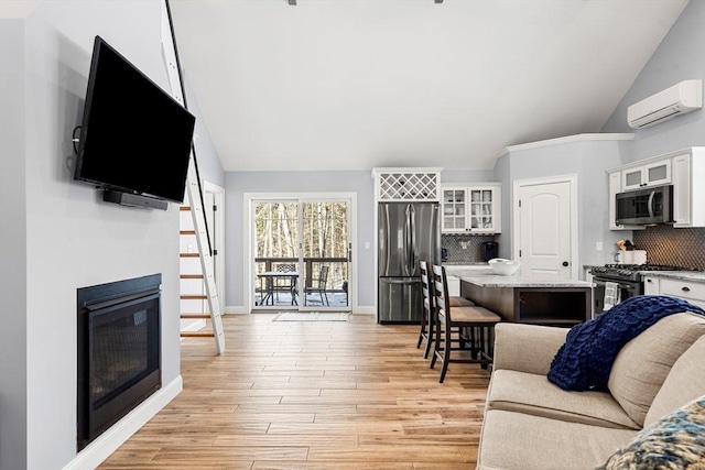 living room with a wall mounted air conditioner, light hardwood / wood-style flooring, and vaulted ceiling