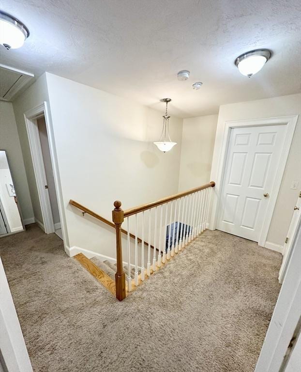 hall with baseboards, carpet floors, attic access, a textured ceiling, and an upstairs landing