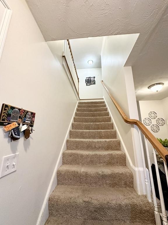 staircase with carpet flooring, baseboards, and a textured ceiling