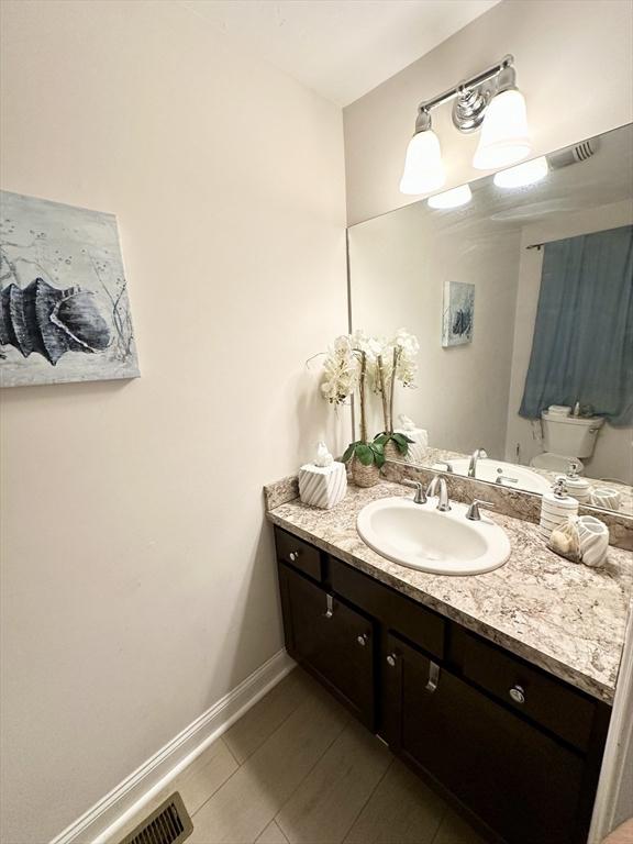 bathroom featuring visible vents, toilet, vanity, and baseboards