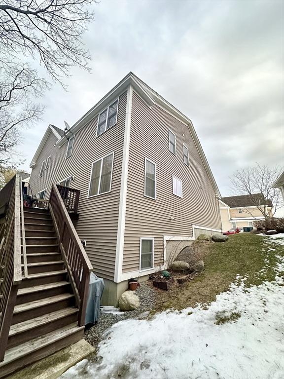 snow covered back of property featuring a deck and stairway